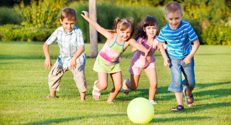 Kinder rennen mit einem Ball über eine Wiese
