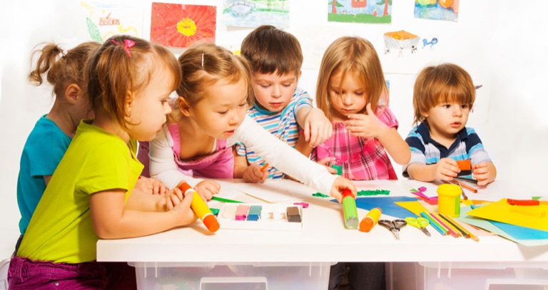 Kinder basteln gemeinsam an einem langen Tisch