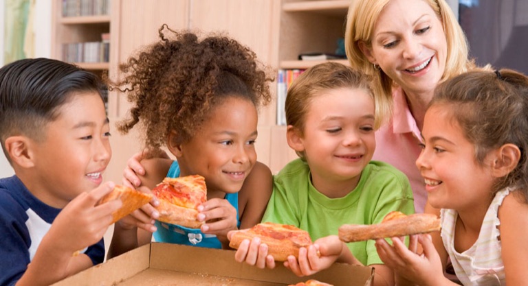 Erzieherin sitzt mit Kindern beim Essen am Tisch