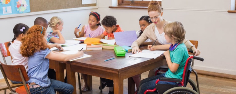Kinder malen gemeinsam am Tisch, eines sitzt im Rollstuhl