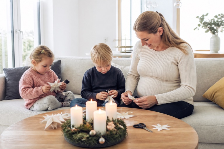 Schwangere bastelt mit zwei Kindern Papiersterne, Adventskranz auf dem Tisch
