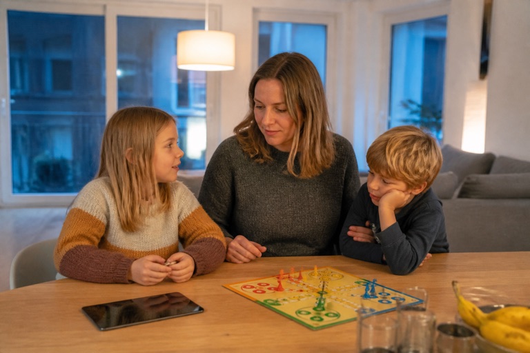 Familie am Abend im Wohnzimmer, Tablet liegt umgedreht auf dem Tisch, Brettspiel daneben