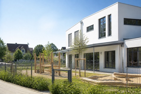 Helles Kita-Gebäude mit Spielplatz und Klettergerüst davor