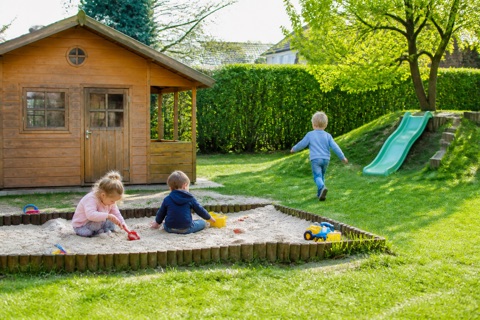 Kinder spielen im Sandkasten eines Kita-Gartens, daneben ein Spielhaus