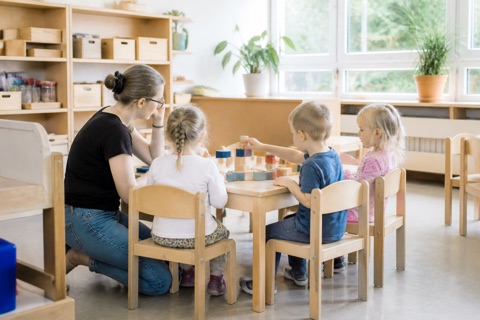 Erzieherin und vier Kinder am Tisch beim Spiel mit Holzbausteinen