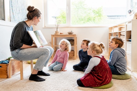 Erzieherin liest vier Kindern aus einem Bilderbuch vor