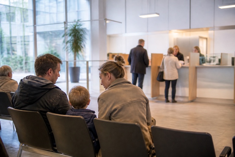 Wartebereich einer Behörde mit einer Familie auf Stühlen