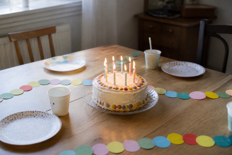 Gedeckter Geburtstagstisch mit Kuchen, Kerzen und Girlande