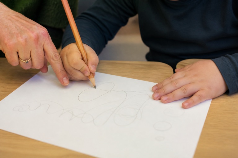 Kinderhand hält einen dicken Stift und zeichnet Linien auf Papier