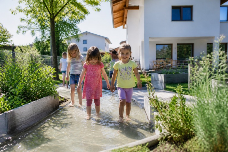 Kinder waten barfuss durch ein flaches Wasserbecken im Kindergartengarten