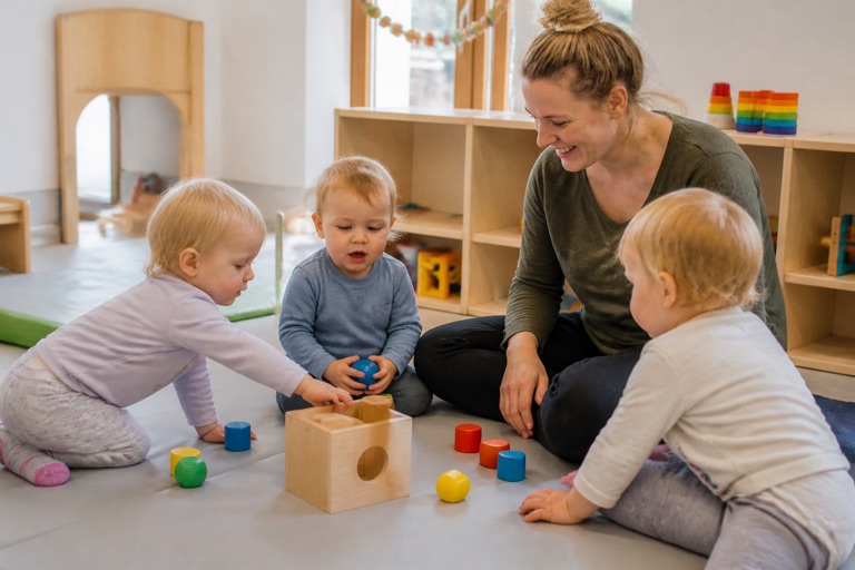 Kleinkinder spielen mit einer Erzieherin auf einer weichen Bodenfläche