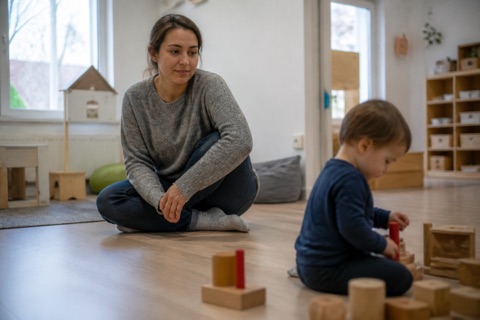 Mutter sitzt im Gruppenraum, während ihr Kind spielt