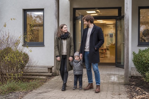 Eltern bringen ihr Kind zum Eingang einer Kindertagesstätte